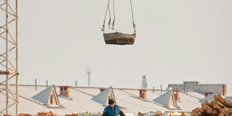 Construction. A man builder walks on the roof of a brick building under construction next to a crane