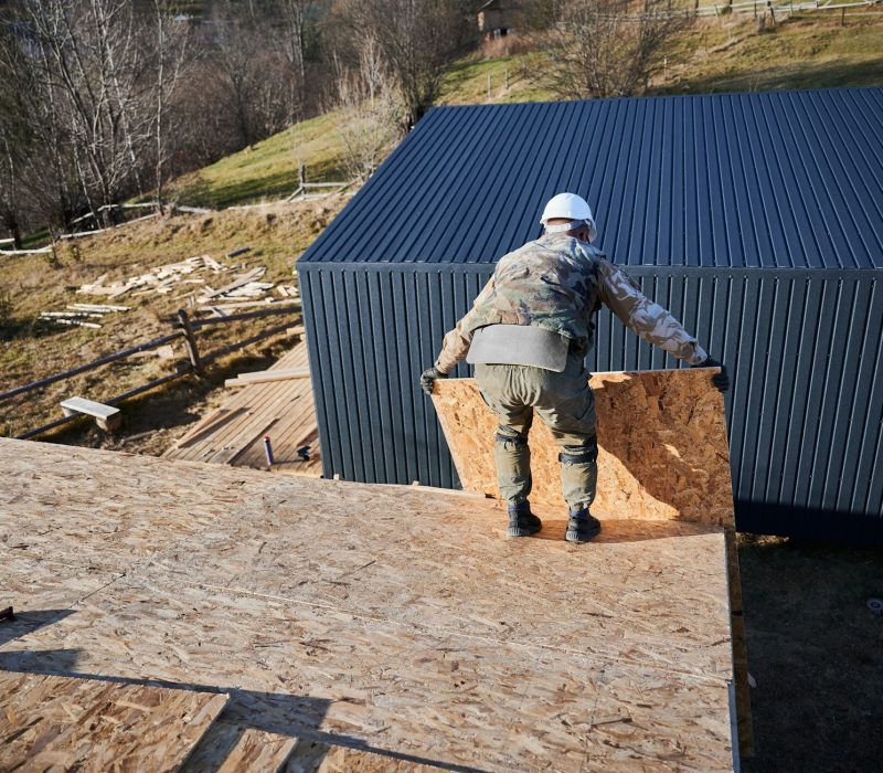Man worker building wooden frame house, mounting wooden OSB board.
