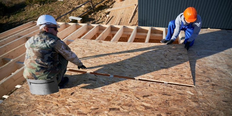 Man worker building wooden frame house, mounting wooden OSB board.