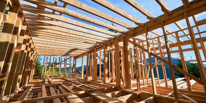 Wooden frame house under construction near forest.